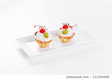 Beautiful cream cakes with cherries and grapes on a plate on a white background 112304806