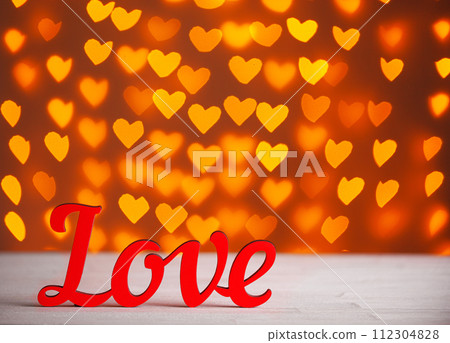 the inscription Love on a wooden background with beautiful hearts made of lights on a blurred background 112304828