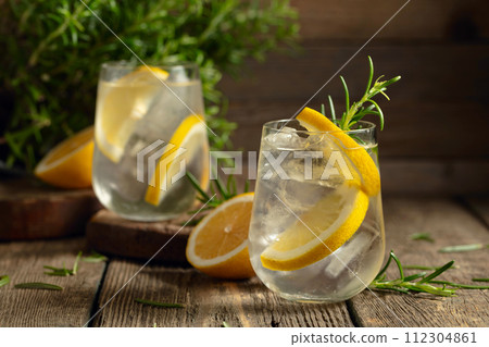 Cocktail gin tonic with ice, lemon, and rosemary on a old wooden table. 112304861