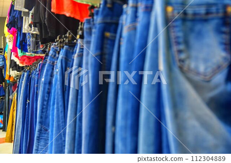 Row of hanged blue jeans in a shop. Clothes store. Shopping in fashion mall. Garments on hangers. Clothes on the store shelves 112304889