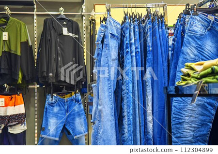 Row of hanged blue jeans in a shop. Clothes store. Shopping in fashion mall. Garments on hangers. Clothes on the store shelves 112304899