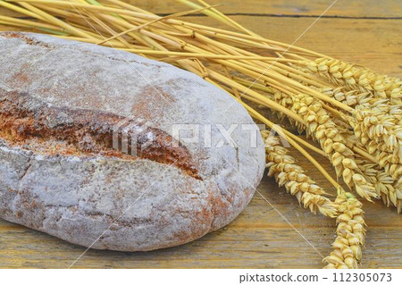 Loaf of bread and ears of grain on wood background. Rustic and rural concept. Close up Loaf of bread and ears of grain on wood background. Rustic and rural concept. Close up 112305073
