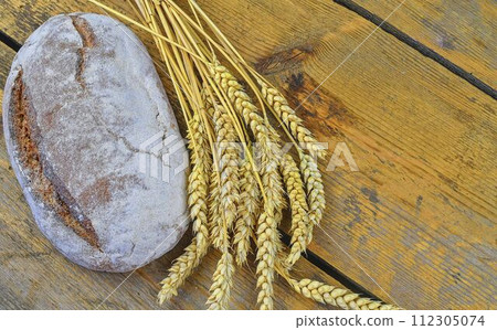 Loaf of bread and ears of grain on wood background. Rustic and rural concept. Copy space Loaf of bread and ears of grain on wood background. Rustic and rural concept. Copy space 112305074