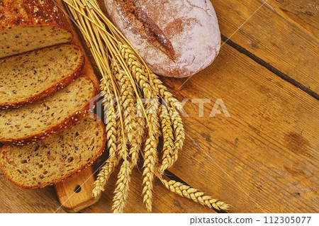 Loafs of bread, slices of bread and ears of grain on wood background. Rustic and rural concept. Close up Loafs of bread, slices of bread and ears of grain on wood background. Rustic and rural concept. Close up 112305077