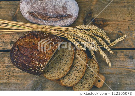 Loafs of bread, slices of bread and ears of grain on wood background. Rustic and rural concept. Close up Loafs of bread, slices of bread and ears of grain on wood background. Rustic and rural concept. Close up 112305078