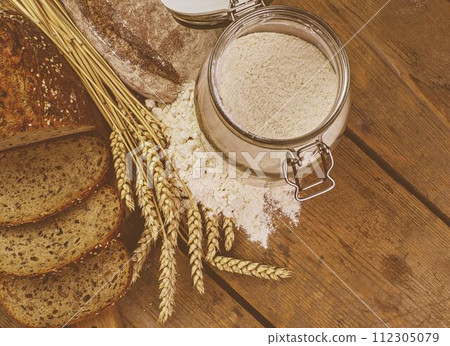 Loafs of bread, slices of bread, wheat flour and ears of grain on wood background. Rustic and rural concept. Close up. Flat lay Loafs of bread, slices of bread, wheat flour and ears of grain on wood background. Rustic and rural concept. Close up. Flat lay 112305079