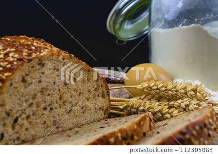 Loafs of bread, slices of bread, wheat flour, eggs and ears of grain on wood background. Rustic and rural concept. Close up. Copy space 112305083