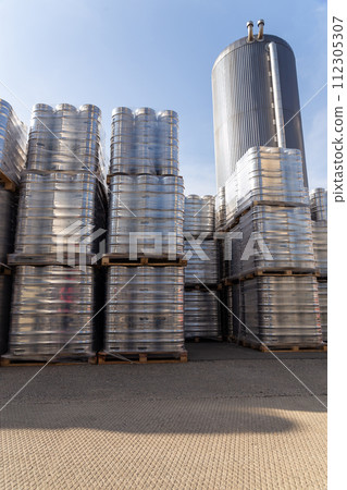 Large amount of aluminium beer kegs stacked on each other with euro palettes and wrapped around with vinyl foil. 112305307