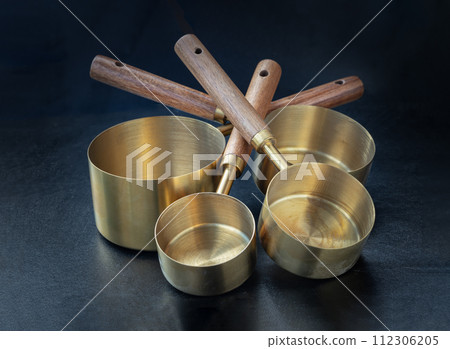 Set of Brass Measuring Cups with Wood Handles with Hanging Hole Design on dark background. Set of Brass Measuring Cups with Wood Handles with Hanging Hole Design on dark background. 112306205