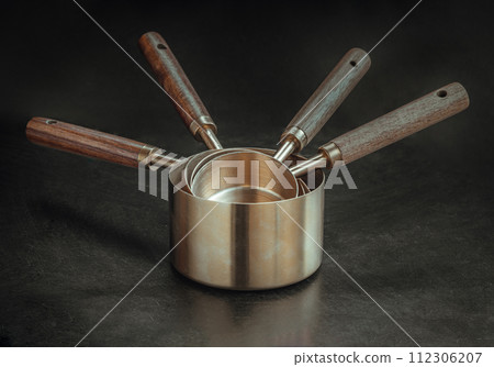 Set of Brass Measuring Cups with Wood Handles with Hanging Hole Design on dark background. Set of Brass Measuring Cups with Wood Handles with Hanging Hole Design on dark background. 112306207