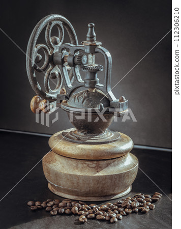 Old original coffee bean original grinder metal shake wheel with hand crank and coffee beans on dark background. Old original coffee bean original grinder metal shake wheel with hand crank and coffee beans on dark background. 112306210