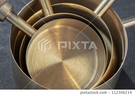 Set of Brass Measuring Cups with Wood Handles with Hanging Hole Design on dark background. 112306214