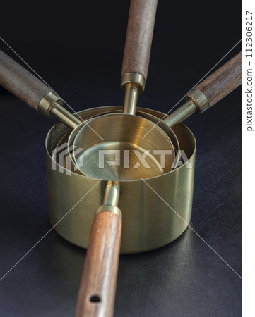 Set of Brass Measuring Cups with Wood Handles with Hanging Hole Design on dark background. 112306217