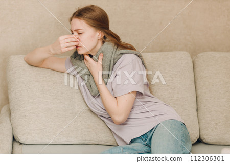 Young woman wearing scarf has flu ill sick disease cold at home indoor on sofa Young woman wearing scarf has flu ill sick disease cold at home indoor on sofa 112306301