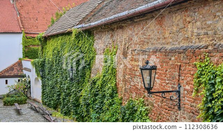 Ivy on red brick wall. Old fashioned urban lighting on red wall. Historical urban backyard Ivy on red brick wall. Old fashioned urban lighting on red wall. Historical urban backyard 112308636