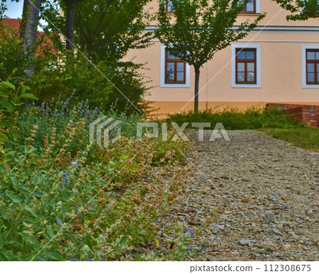 Urban gravel path. Soft colors. Flowers and building on background. Selective focus Urban gravel path. Soft colors. Flowers and building on background. Selective focus 112308675
