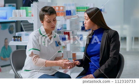 Healthcare expert clipping asian patient finger using pulse oximeter, monitoring level of blood oxygen saturation and heart rate during appointment in chemist shop offering full range of services 112310733
