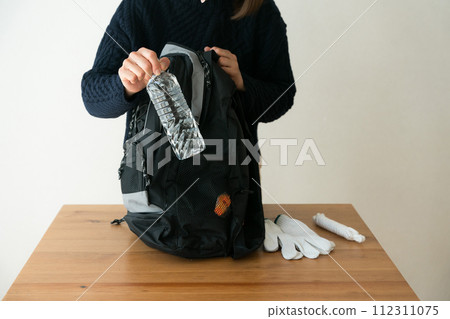 一名婦女將塑膠瓶放入防災背包中 一名婦女將塑膠瓶放入防災背包中 112311075