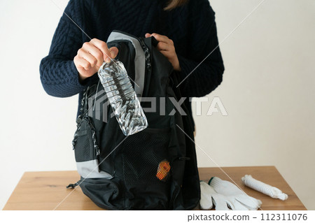 一名婦女將塑膠瓶放入防災背包中 112311076