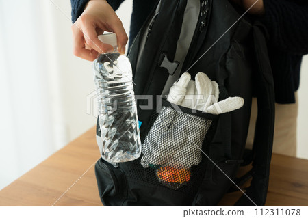 一名婦女將塑膠瓶放入防災背包中 112311078