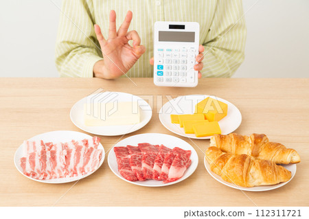 A woman making a circle sign while holding foods containing a lot of fat and a calculator A woman making a circle sign while holding foods containing a lot of fat and a calculator 112311721