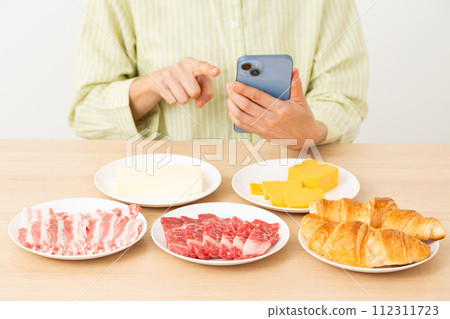A woman with fat-rich foods and a smartphone 112311723