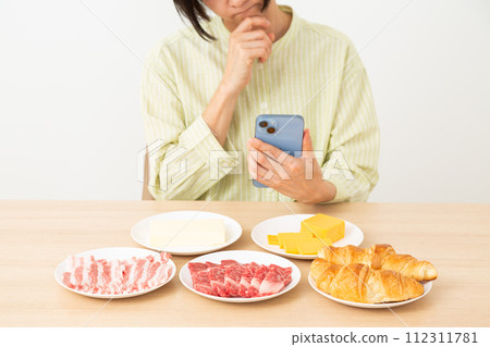 A woman worries about eating foods that contain a lot of fat and using a smartphone. 112311781