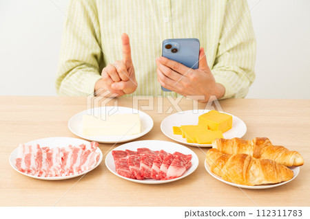 A woman holding a food containing a lot of fat and a smartphone and raising her index finger 112311783