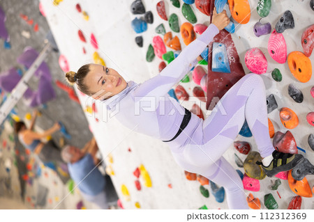 Adult woman practicing rock climbing on climbing wall Adult woman practicing rock climbing on climbing wall 112312369