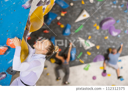 Focused woman climbing without ropes and harnesses on artificial bouldering wall Focused woman climbing without ropes and harnesses on artificial bouldering wall 112312375