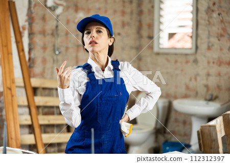 Portrait of confident female foreman in blue overalls in building under construction Portrait of confident female foreman in blue overalls in building under construction 112312397