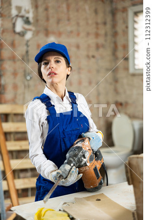 Female contractor standing with demolition hammer inside building under construction Female contractor standing with demolition hammer inside building under construction 112312399