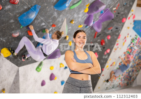 Portrait of slender smiling woman climber on background of climbing wall Portrait of slender smiling woman climber on background of climbing wall 112312403