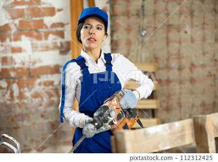 Female contractor standing with demolition hammer inside building under construction Female contractor standing with demolition hammer inside building under construction 112312425
