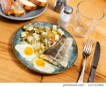 There is plate with fried cod fillet and stewed vegetable on wooden table. 112312468