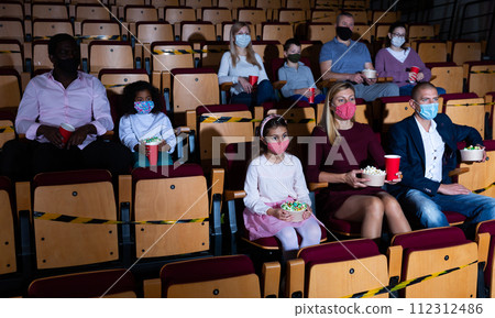 Family with child wearing protective masks eating popcorn and watching a movie in cinema 112312486