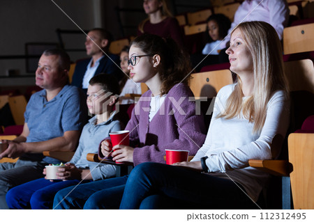 Friendly family sitting with popcorn and drinks in cinema 112312495