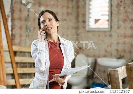 Woman talking on a mobile phone in house under construction Woman talking on a mobile phone in house under construction 112312597