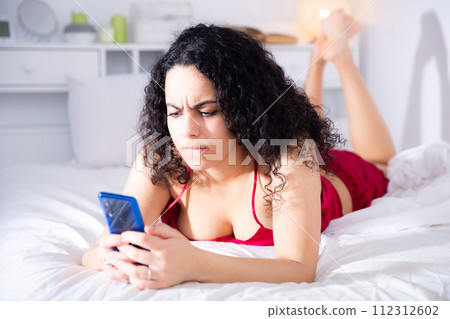 Sexy girl in red lingerie with mobile phone on bed Sexy girl in red lingerie with mobile phone on bed 112312602