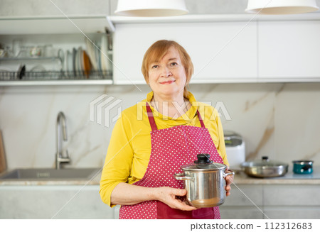 Adult woman in apron posing with saucepan Adult woman in apron posing with saucepan 112312683