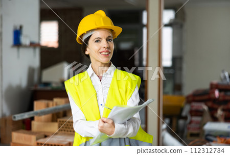 Smiling female civil engineer standing with papers at construction site 112312784