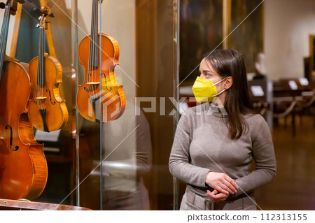 Woman in mask viewing collections of ancient musical instruments in museum Woman in mask viewing collections of ancient musical instruments in museum 112313155