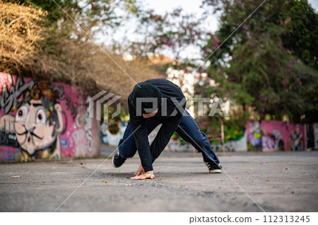 A talented and energetic Asian male hiphop dancer in fashionable clothes is dancing on the street. 112313245