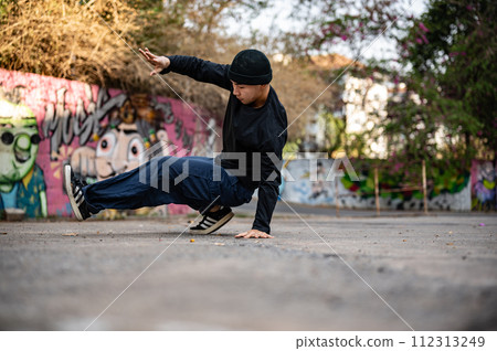 A cool Asian male breakdancer is performing his breakdance on the street, enjoying with the rhythm. 112313249
