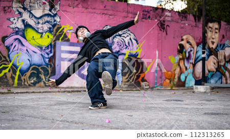 A cool, hipster Asian man hiphop dancer is dancing on the street, trying to spin his body. 112313265