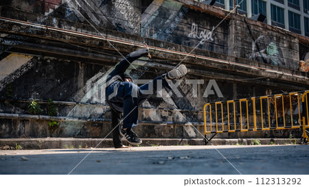A cool Asian male b-boy dancer is dancing on the street with cool street graffiti on the wall. 112313292