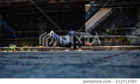 A cool, talented Asian male hiphop dancer is breakdancing on the street in an abandoned street. A cool, talented Asian male hiphop dancer is breakdancing on the street in an abandoned street. 112313307