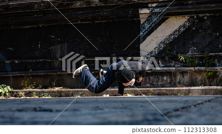 A cool, talented Asian male hiphop dancer is breakdancing on the street in an abandoned street. 112313308