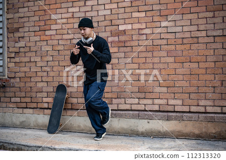 A cool Asian man in fashionable clothes is dancing on the street, practicing his breakdance outdoors 112313320