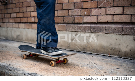 A close-up image of a male skater's feet riding on a skateboard on the street. 112313327
